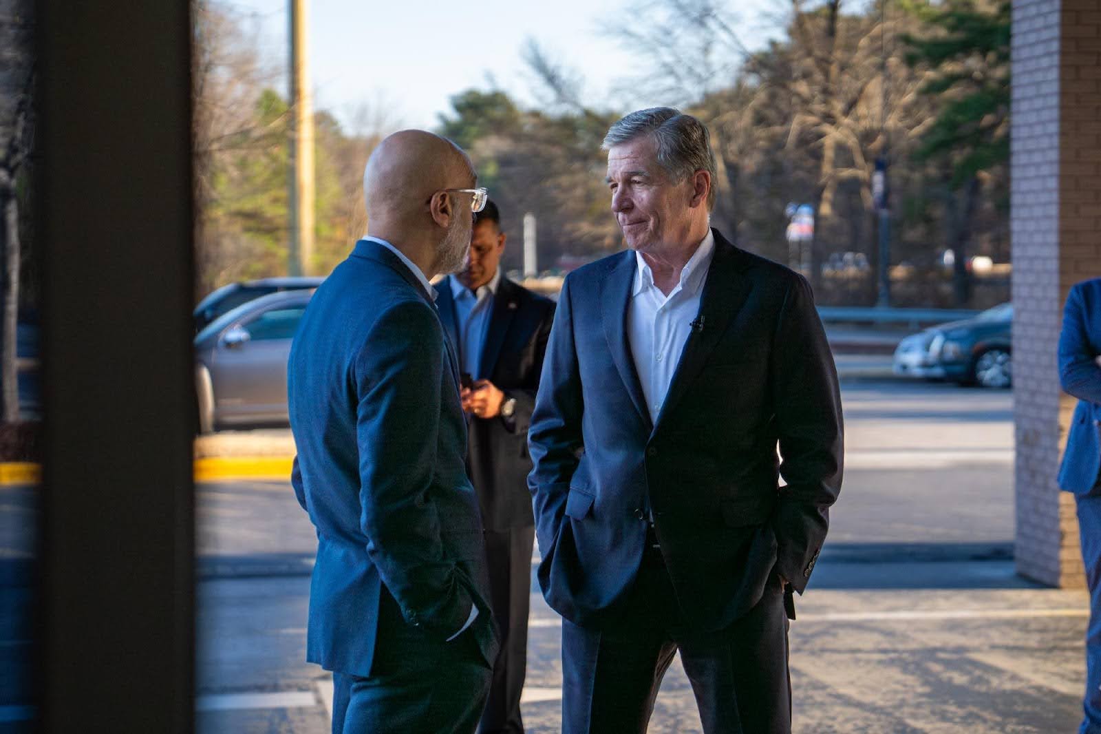 Roy speaks with someone from Rocky Mount, NC. Both are wearing dark suits and button-down shirts.
